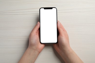Photo of Woman holding smartphone with blank screen at white wooden table, top view. Mockup for design