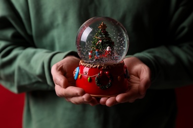 Photo of Man holding snow globe with Christmas tree, closeup