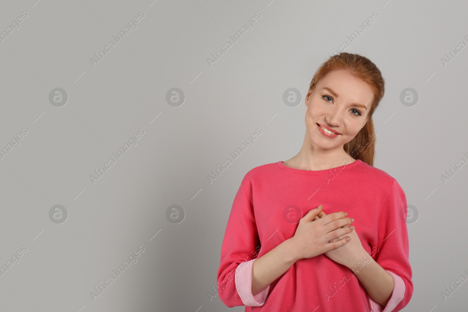 Photo of Beautiful grateful woman with hands on chest against light grey background. Space for text