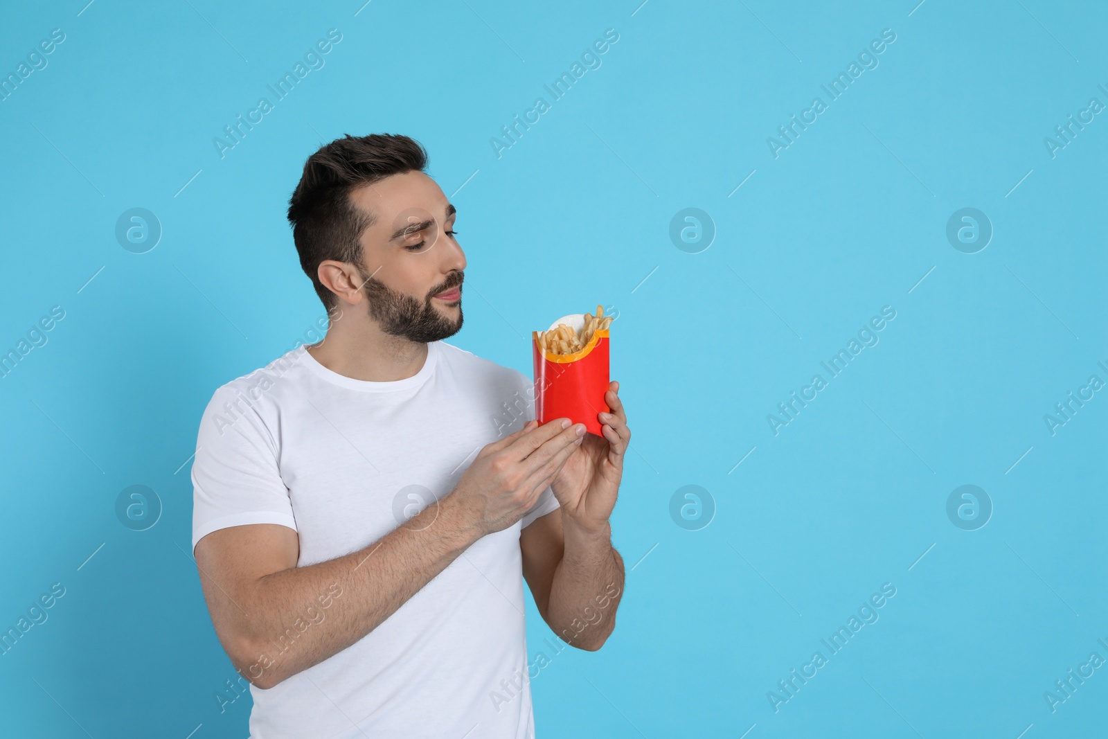 Photo of Man with French fries on light blue background, space for text