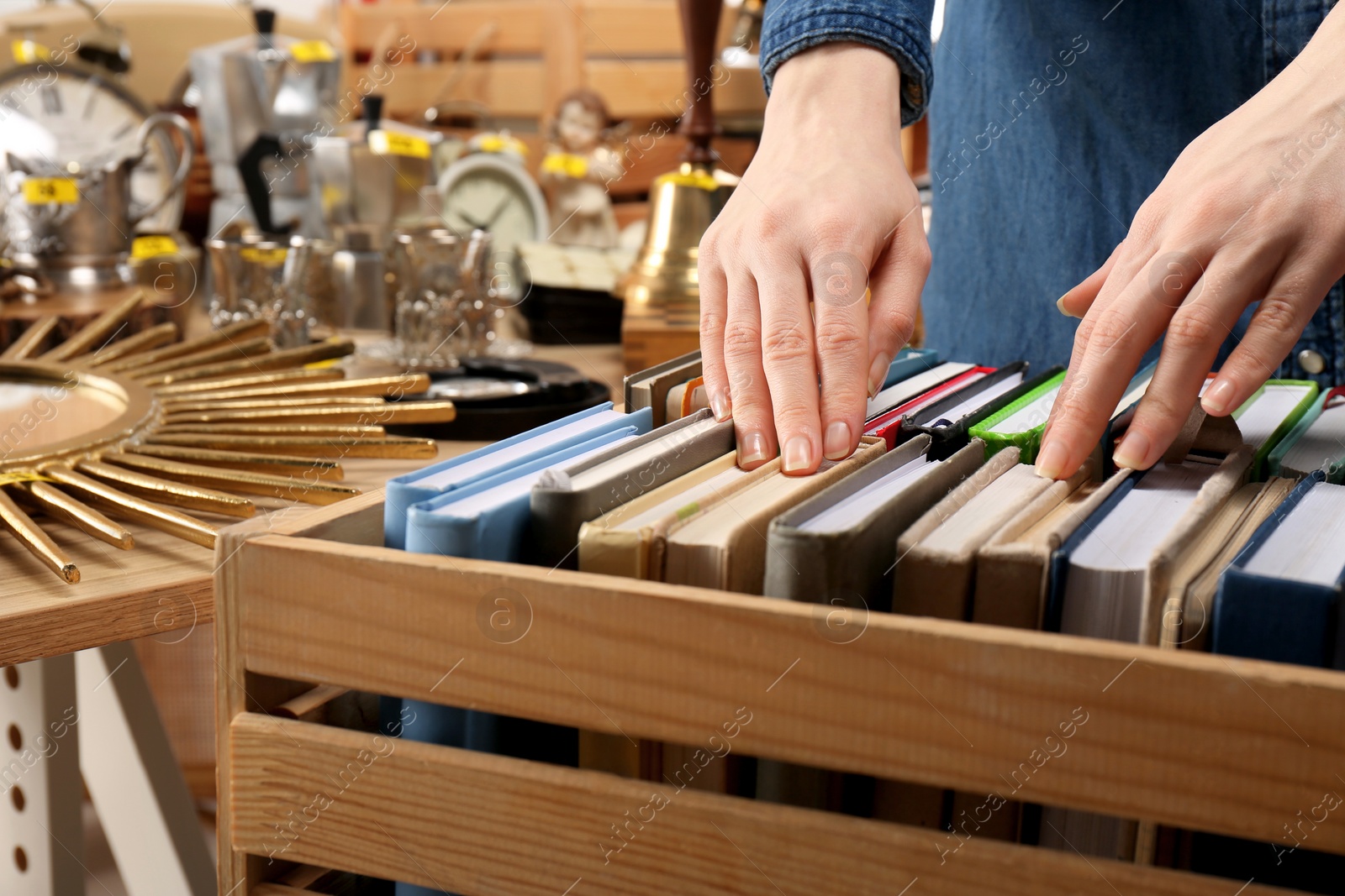 Photo of Woman choosing book near table with different stuff indoors, closeup. Garage sale