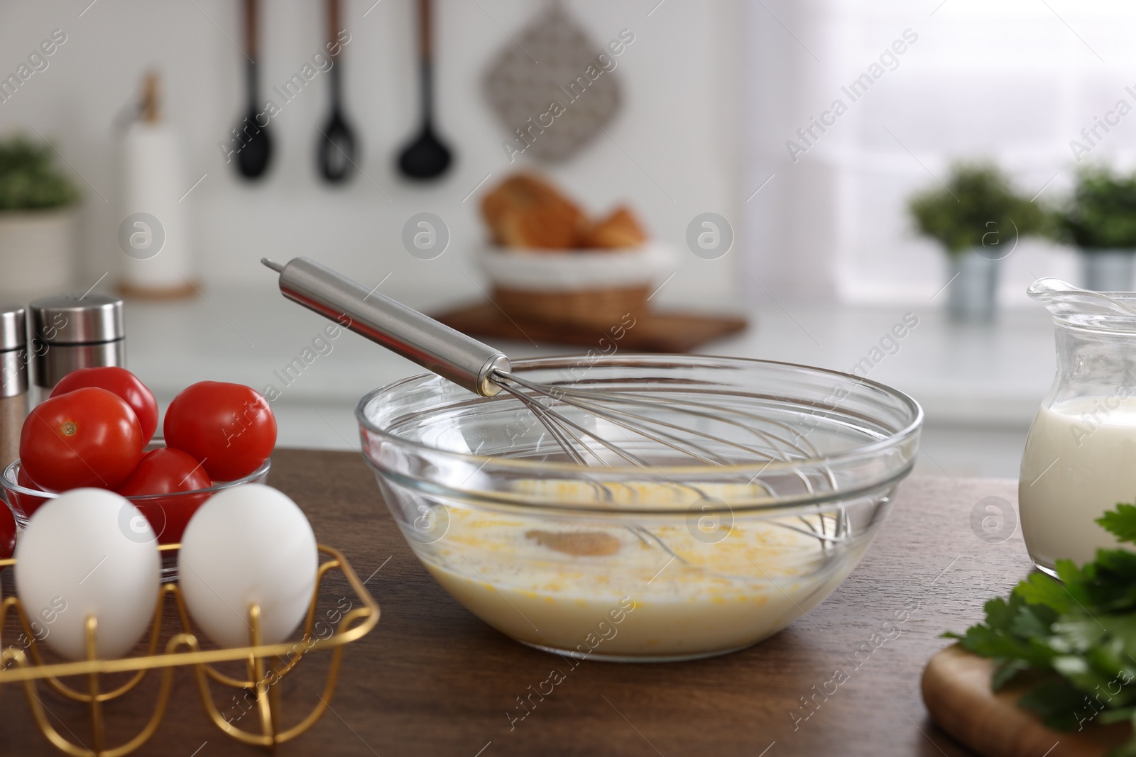 Photo of Whisk, bowl, beaten eggs and other ingredients on wooden table indoors