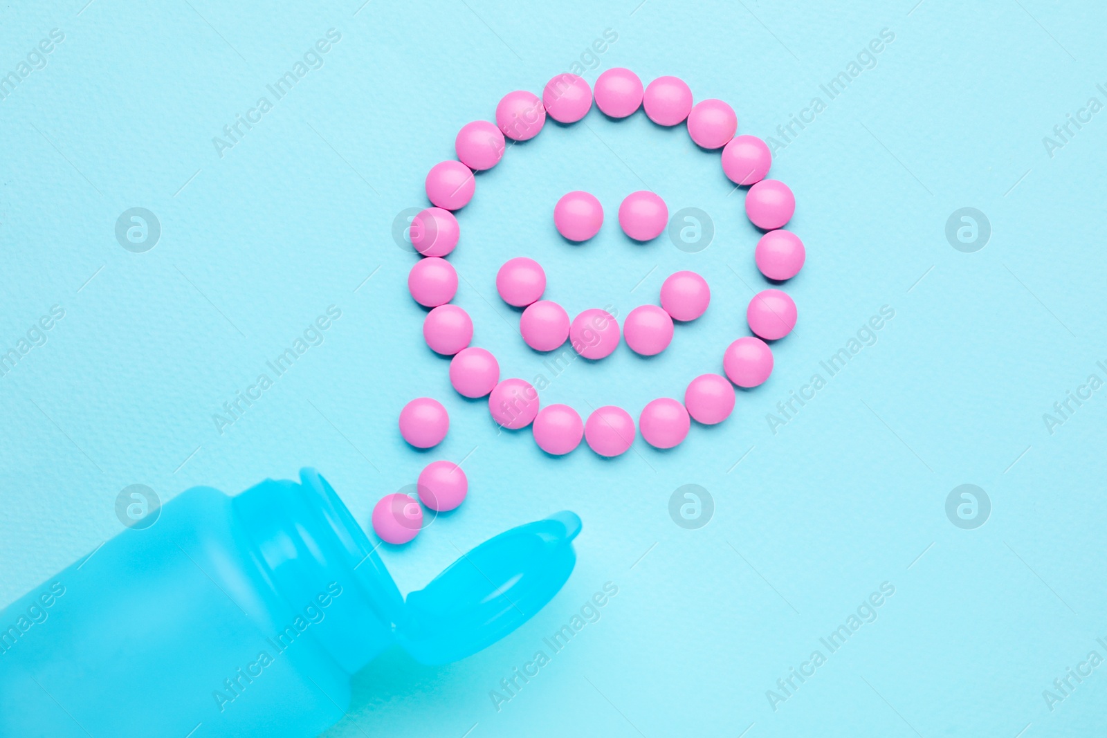 Photo of Happy emoticon made of antidepressants and medical bottle on light blue background, flat lay