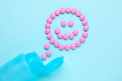 Happy emoticon made of antidepressants and medical bottle on light blue background, flat lay