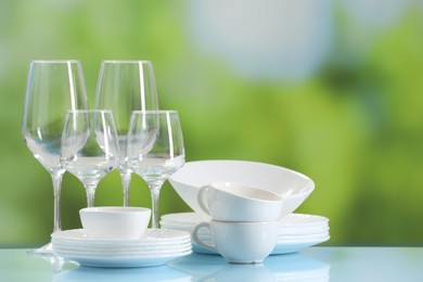 Photo of Set of many clean dishware and glasses on light blue table against blurred green background. Space for text