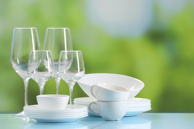 Set of many clean dishware and glasses on light blue table against blurred green background. Space for text