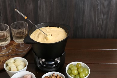 Photo of Fondue pot with tasty melted cheese, forks, wine and different snacks on wooden table