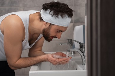 Man with headband washing his face in bathroom