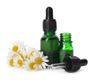 Chamomile flowers and cosmetic bottles of essential oil on white background