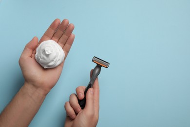 Photo of Man holding shaving foam and razor on light blue background, top view. Space for text