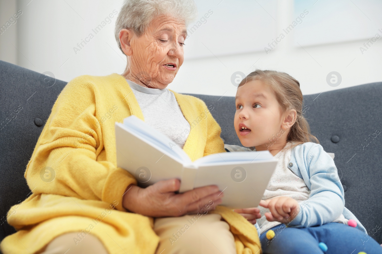 Photo of Cute girl and her grandmother reading book at home