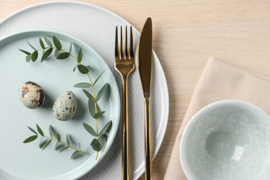 Festive Easter table setting with quail eggs on wooden background, flat lay.