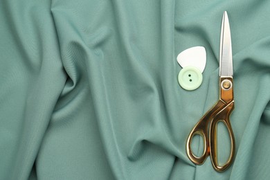 Photo of Scissors, button and tailor's chalk on green fabric, flat lay. Space for text