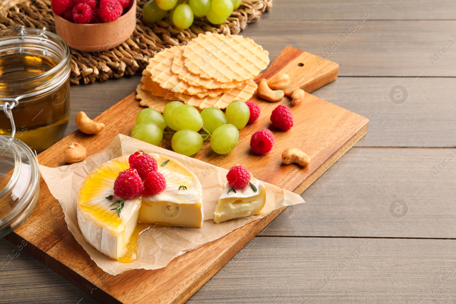 Photo of Brie cheese served with berries and honey on wooden table. Space for text