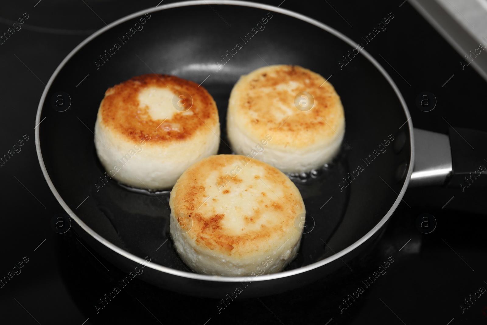 Photo of Delicious cottage cheese pancakes in frying pan on cooktop, closeup