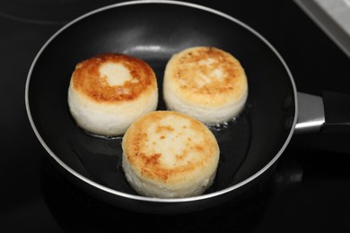 Photo of Delicious cottage cheese pancakes in frying pan on cooktop, closeup