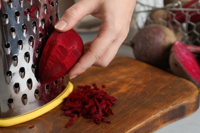 Photo of Woman grating fresh red beet at table, closeup