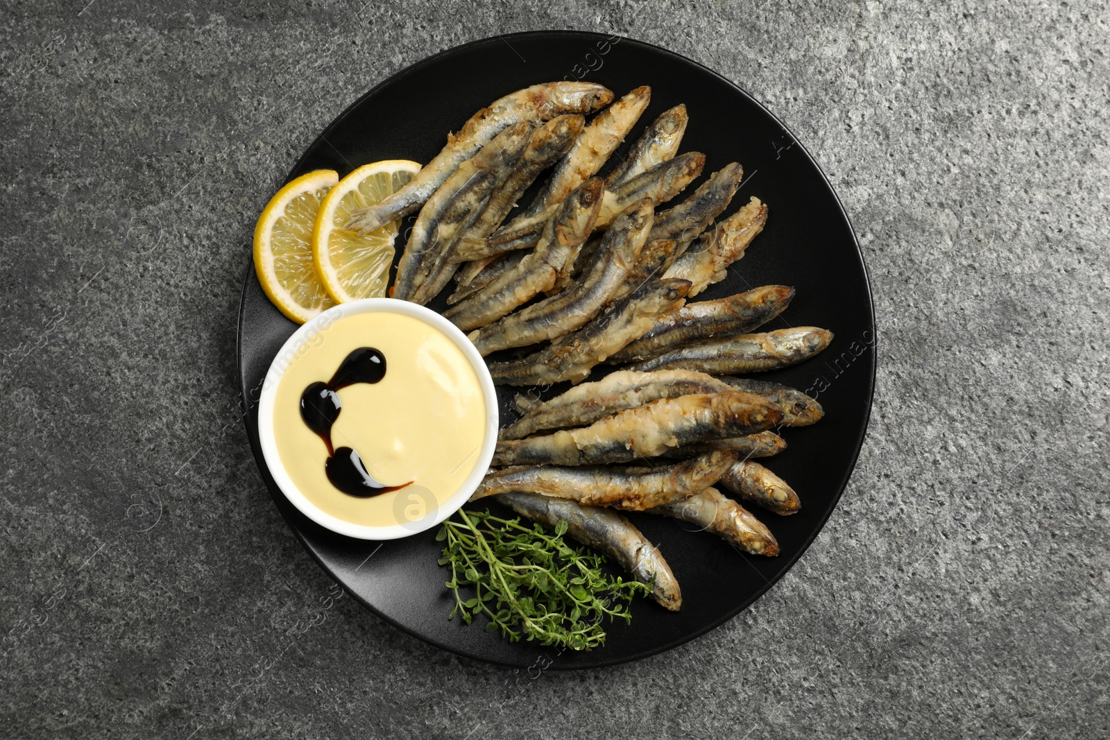 Photo of Plate with delicious fried anchovies, lemon, microgreens and sauce on grey table, top view