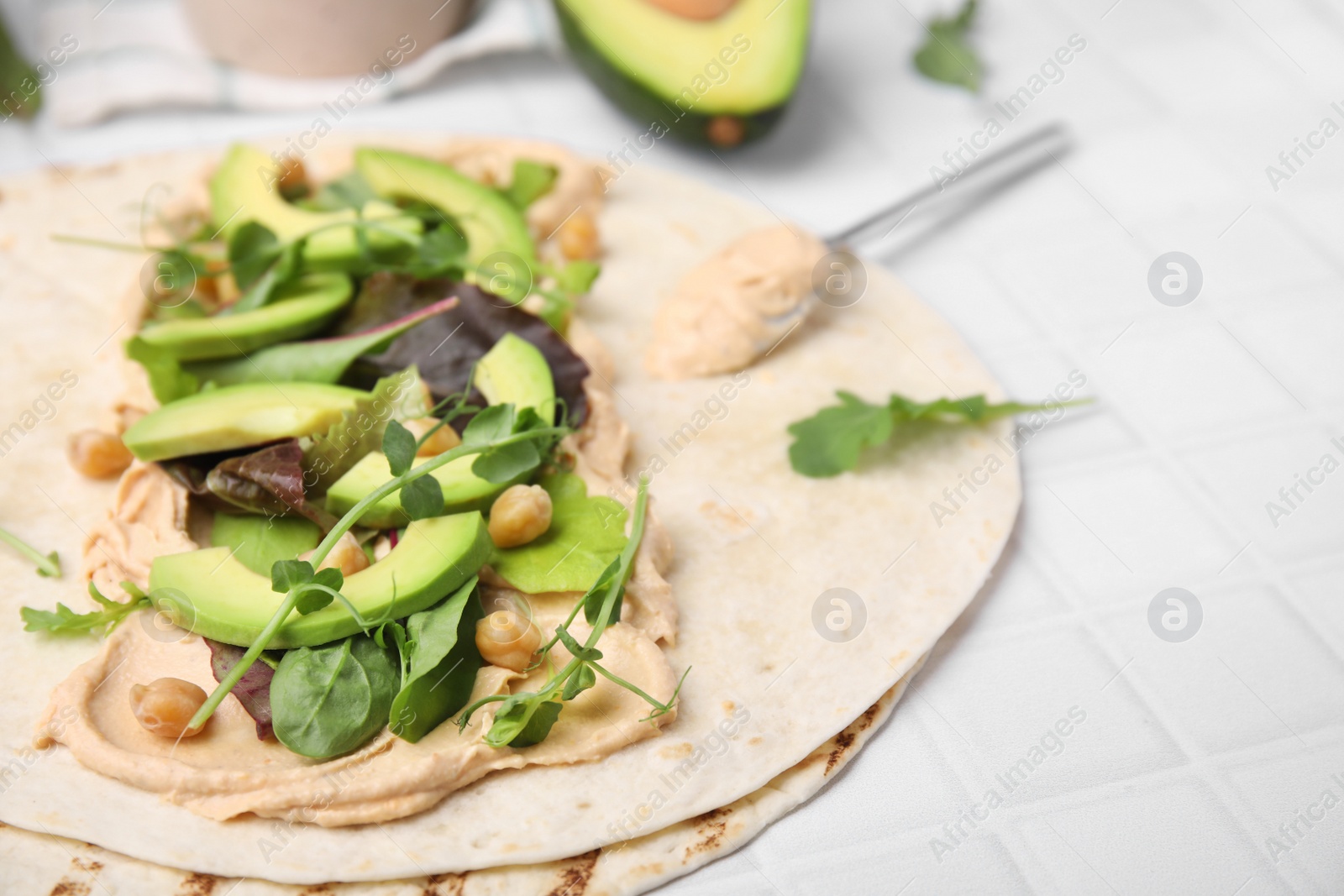 Photo of Tortilla with hummus and vegetables on white table, closeup. Space for text
