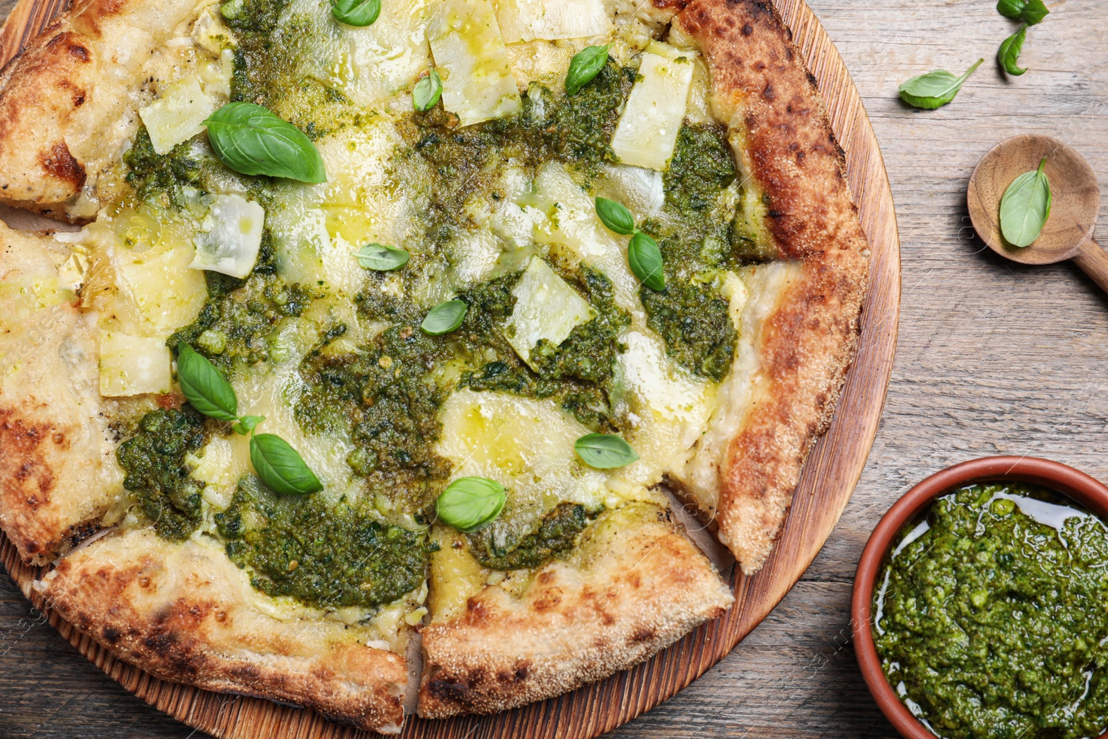 Photo of Delicious pizza with pesto, cheese and basil served on wooden table, flat lay