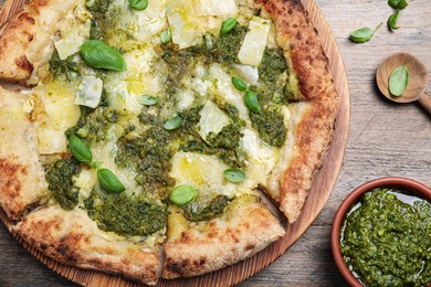 Delicious pizza with pesto, cheese and basil served on wooden table, flat lay