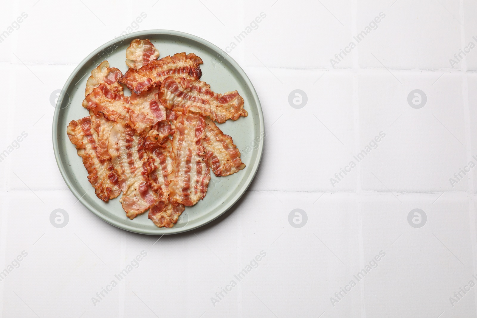 Photo of Delicious fried bacon slices on white wooden table, top view. Space for text