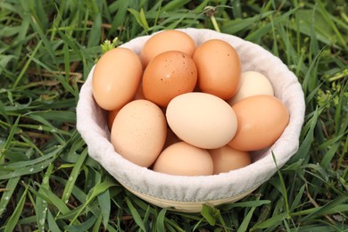 Fresh chicken eggs in basket on green grass outdoors