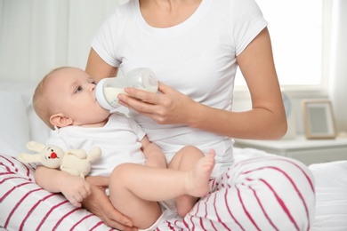 Photo of Lovely mother holding and feeding her baby from bottle on bed at home