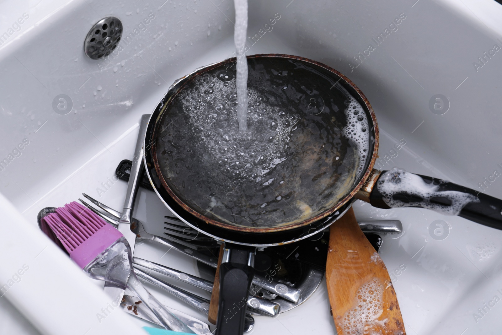 Photo of Pouring water on dirty kitchenware and cutlery in sink