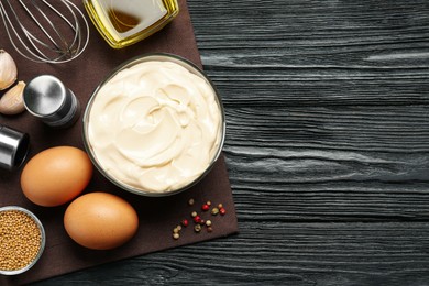 Photo of Glass bowl with fresh mayonnaise and ingredients on black wooden table, top view. Space for text