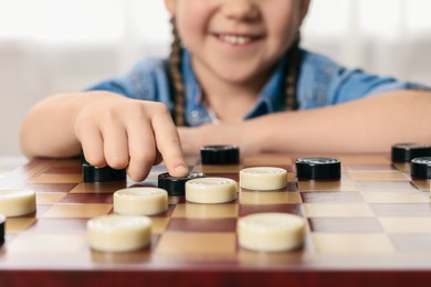 Photo of Playing checkers. Little girl thinking about next move at table in room, closeup