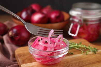 Photo of Fork with tasty pickled onion slices  over bowl on wooden cutting board