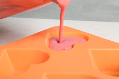 Photo of Pouring smoothie into ice cube tray on table, closeup