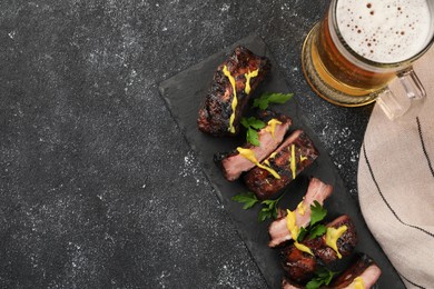 Photo of Mug with beer and delicious grilled ribs on dark grey textured table, flat lay. Space for text