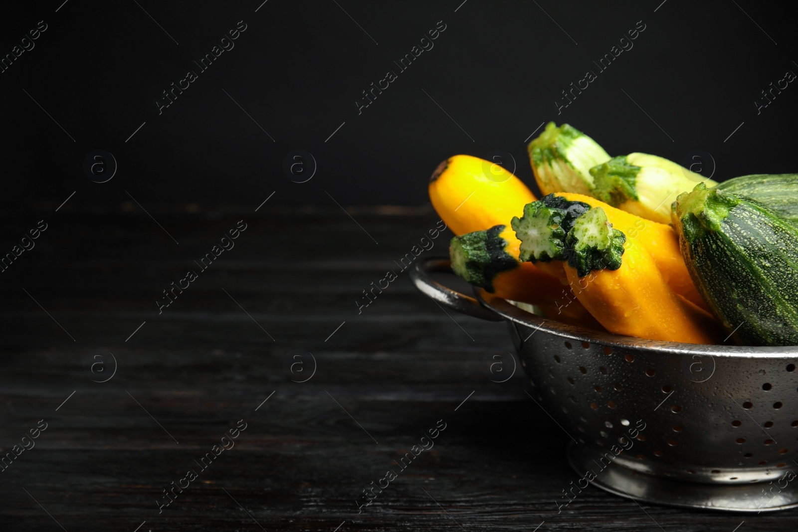 Photo of Colander with fresh ripe zucchini on black wooden table. Space for text