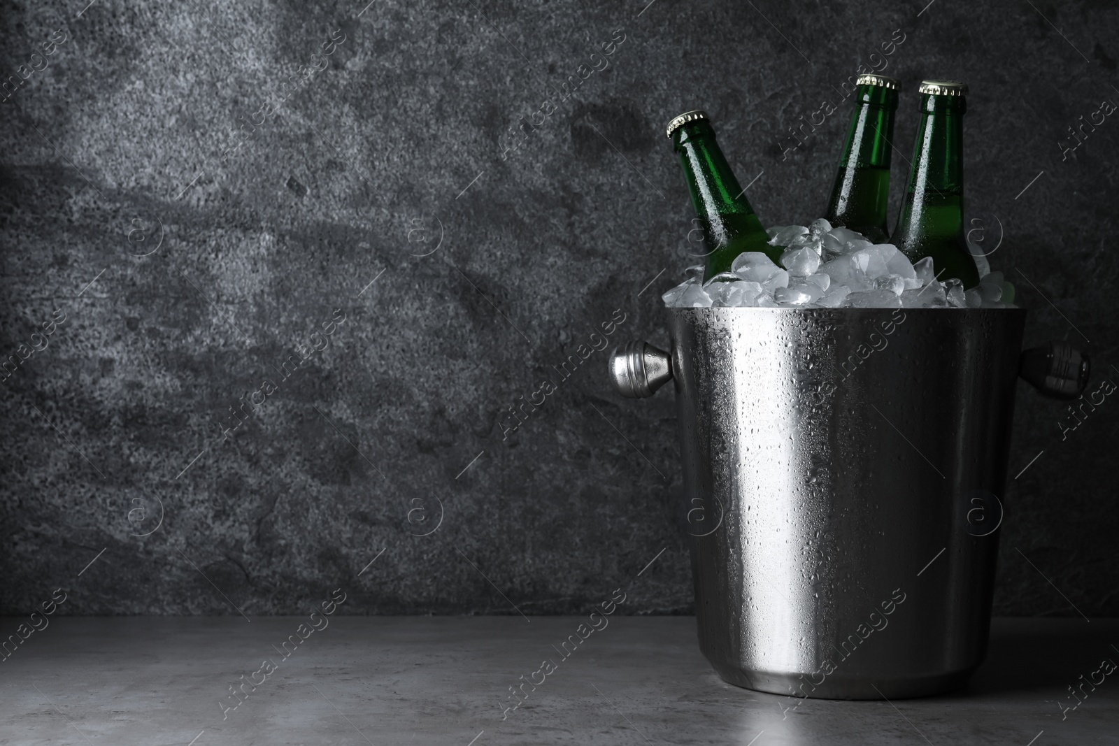 Photo of Metal bucket with beer and ice cubes on grey table. Space for text