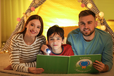 Family with flashlight reading book at home