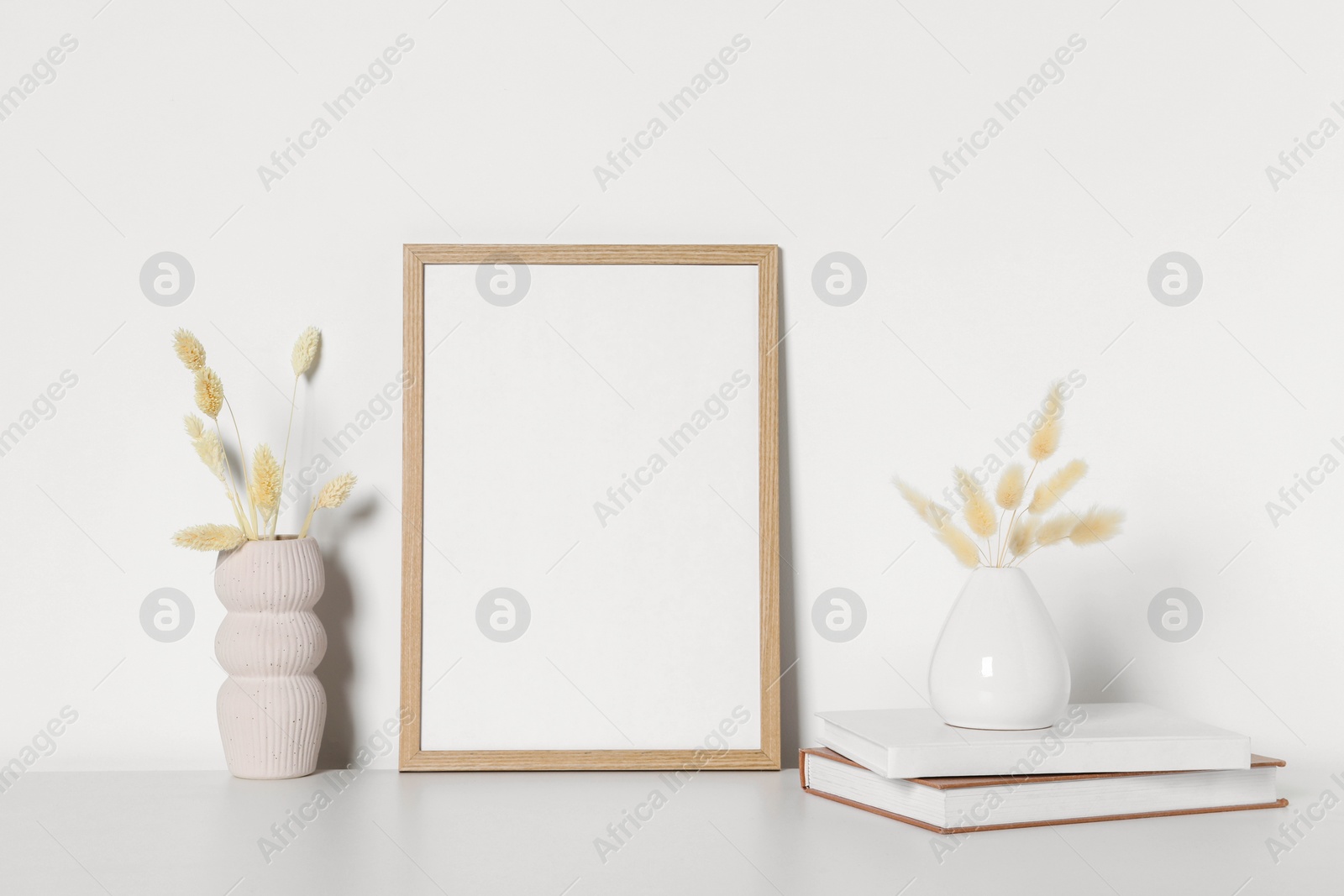 Photo of Empty photo frame and vases with dry decorative spikes on white table. Mockup for design