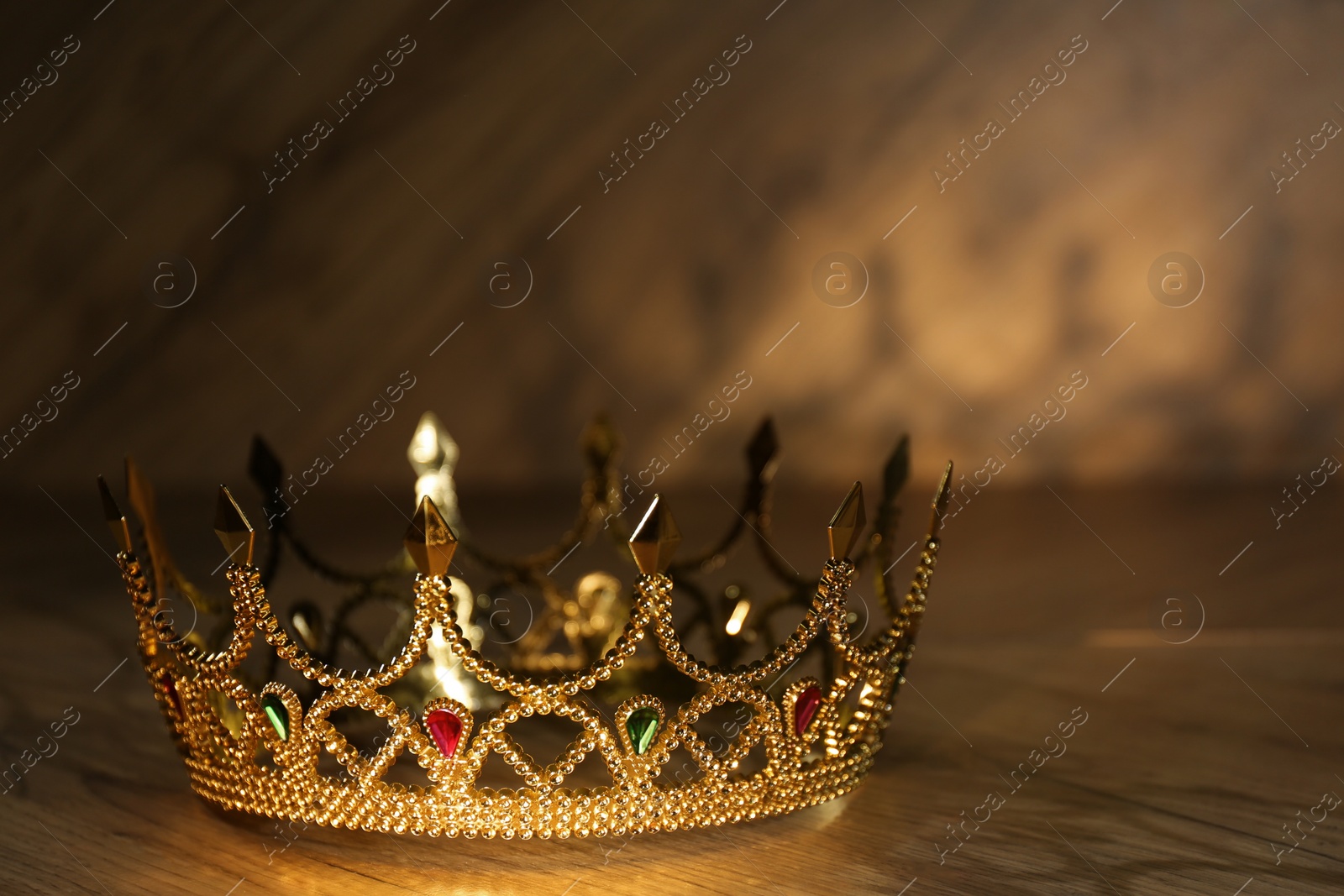 Photo of Beautiful golden crown with gems on wooden table. Fantasy item