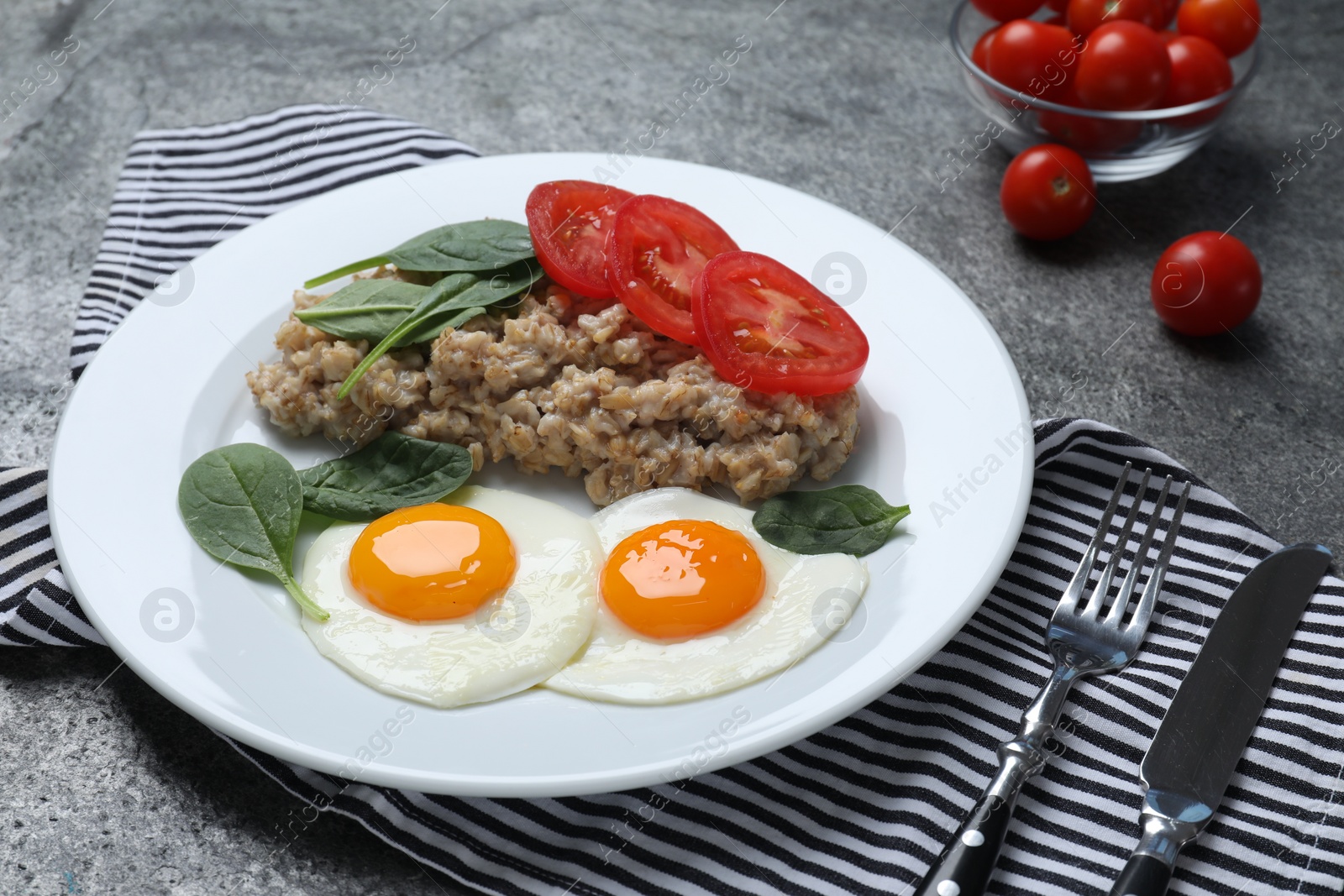 Photo of Delicious boiled oatmeal with fried eggs, tomato and basil served on grey table