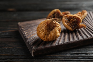 Photo of Wooden board with tasty dried figs on black table, closeup
