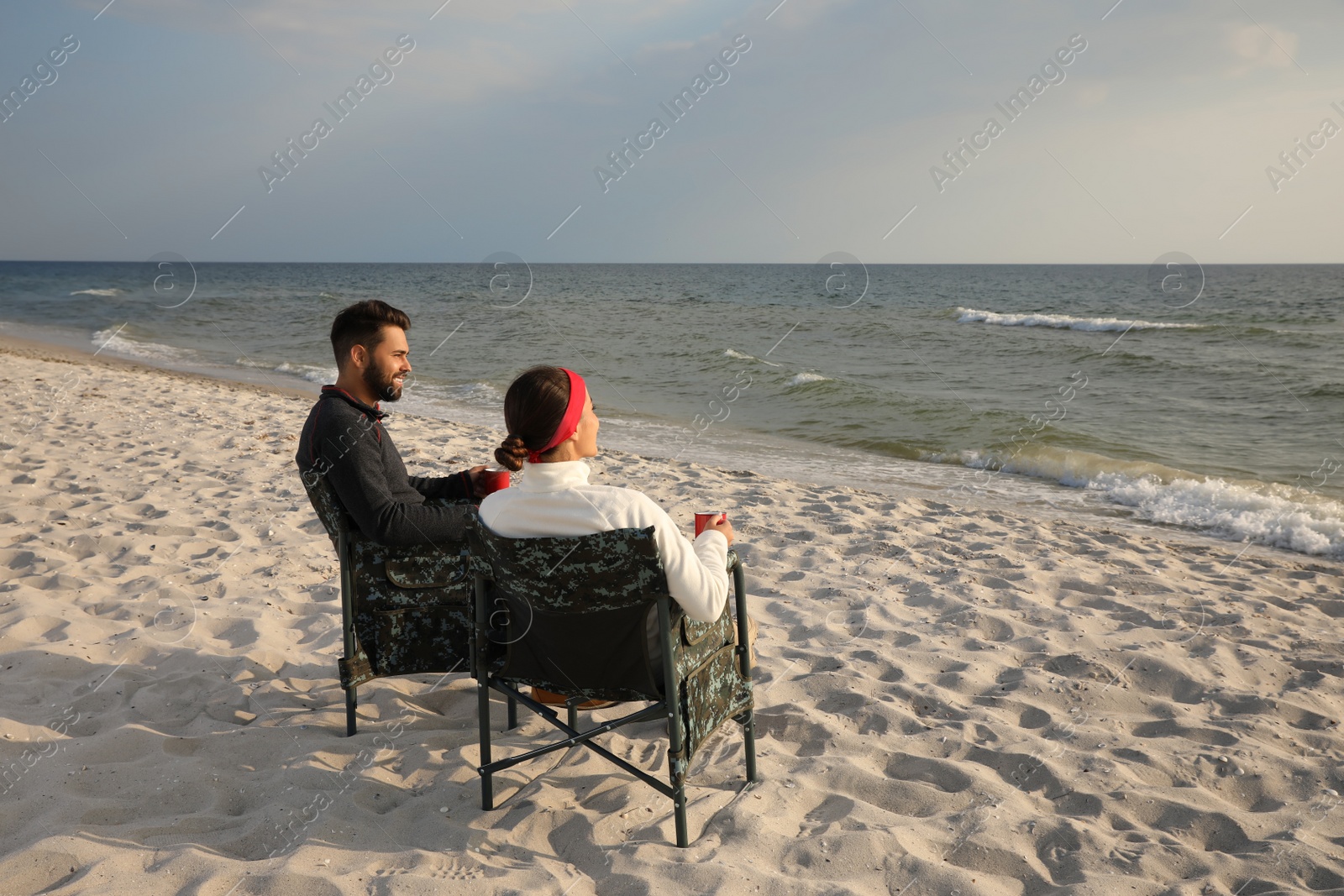 Photo of Couple sitting in camping chairs and enjoying seascape on beach