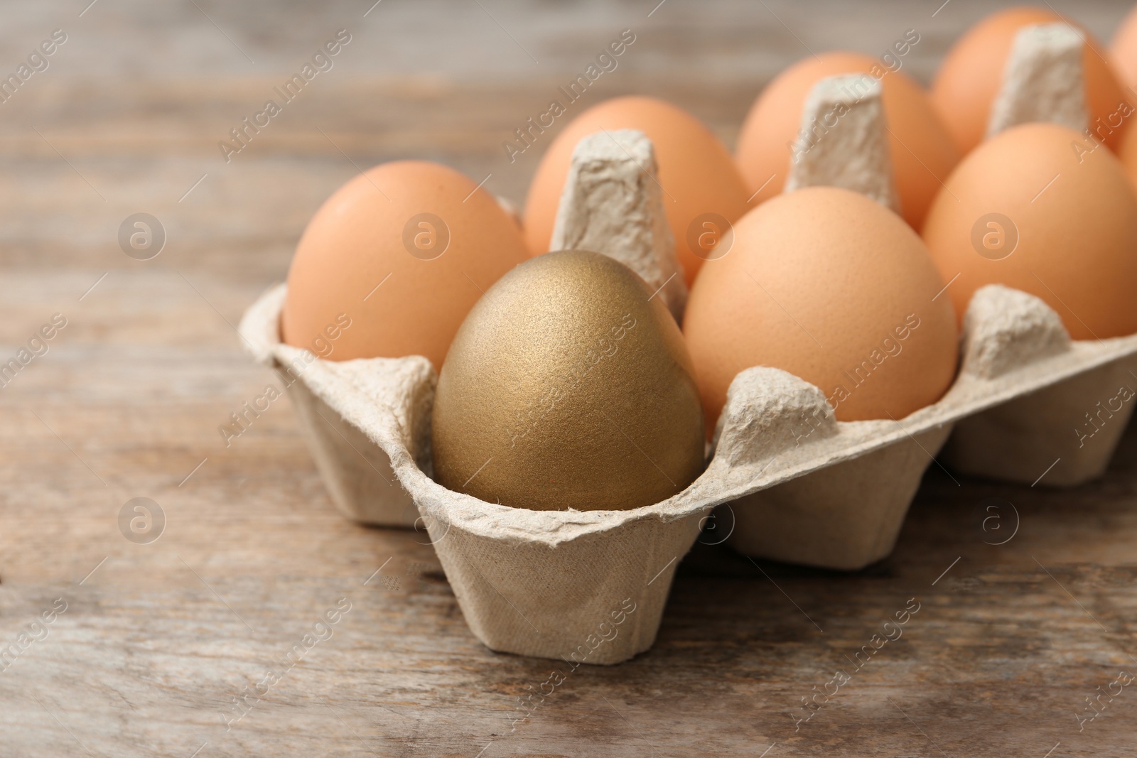 Photo of Golden egg among others in carton on wooden background
