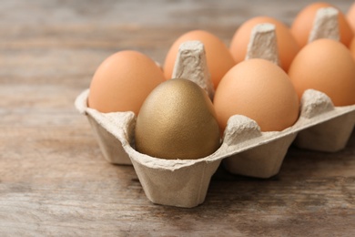 Golden egg among others in carton on wooden background