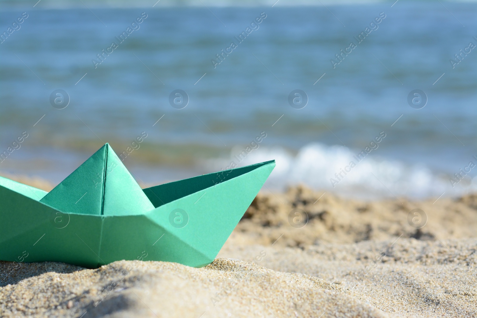 Photo of Green paper boat near sea on sunny day, closeup. Space for text