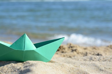 Photo of Green paper boat near sea on sunny day, closeup. Space for text
