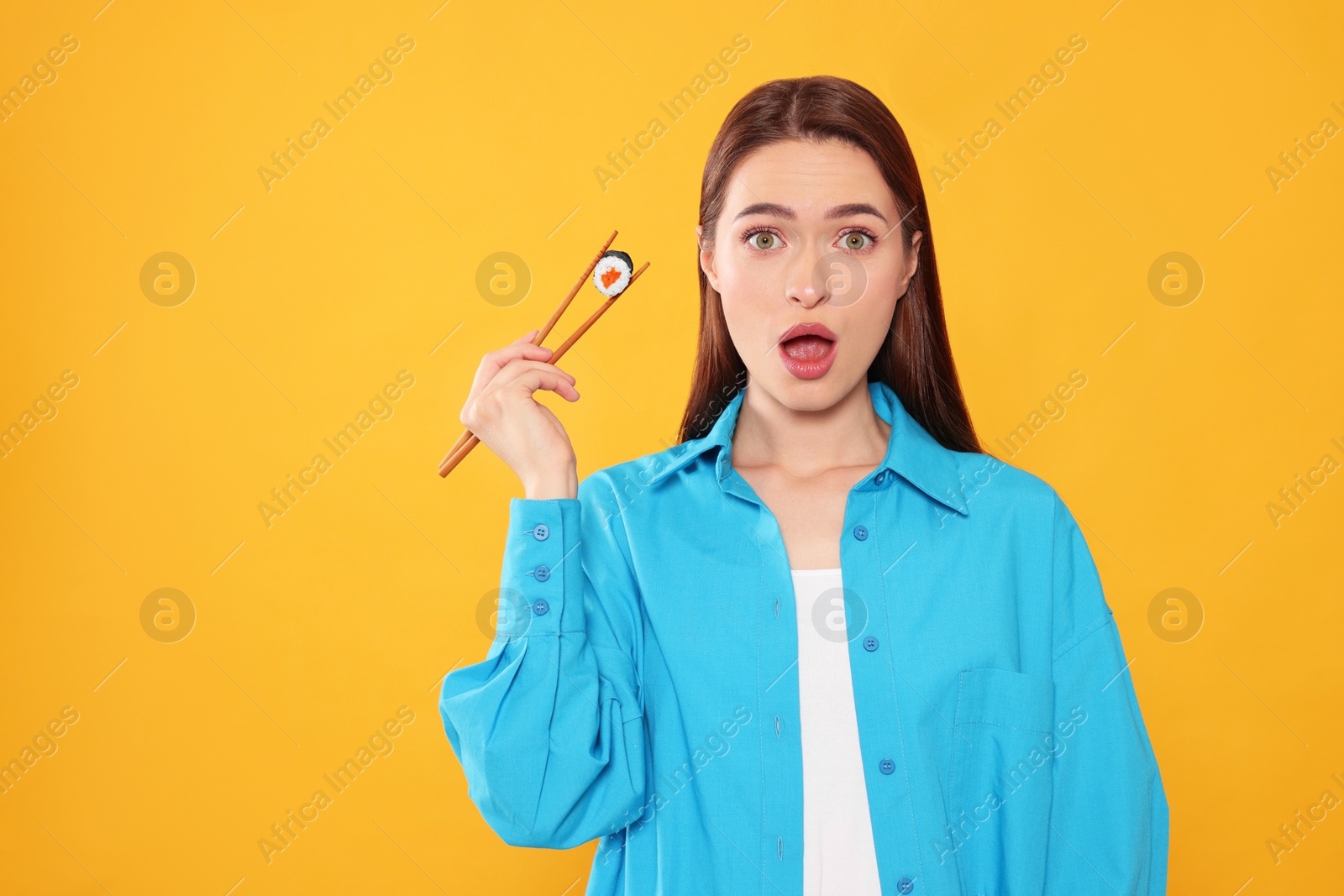 Photo of Emotional young woman holding sushi roll with chopsticks on orange background. Space for text