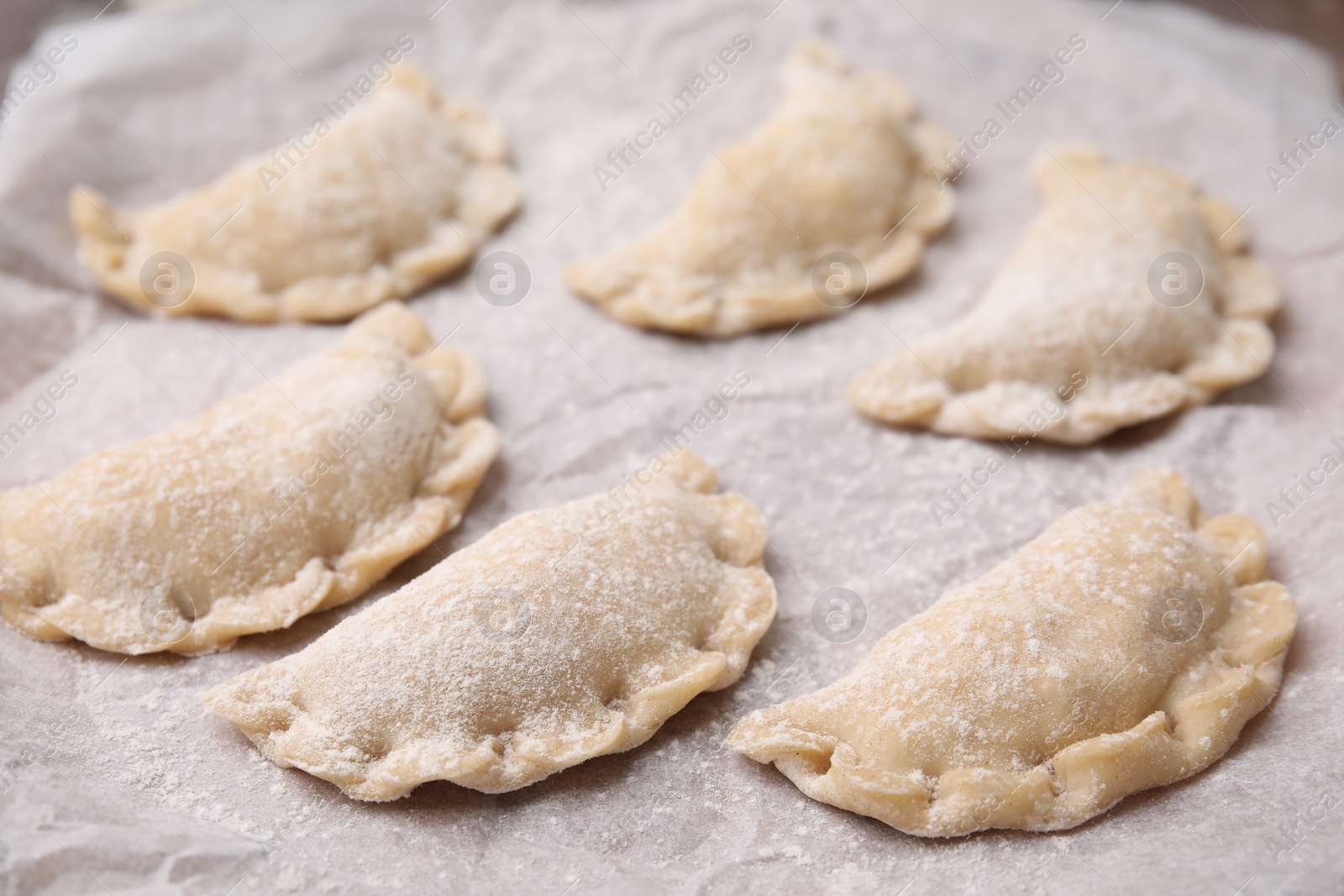 Photo of Raw dumplings (varenyky) with tasty filling on parchment, closeup. Traditional Ukrainian dish