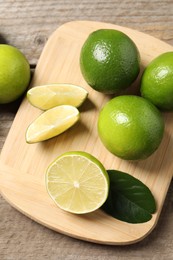 Whole and cut fresh limes on wooden table, flat lay