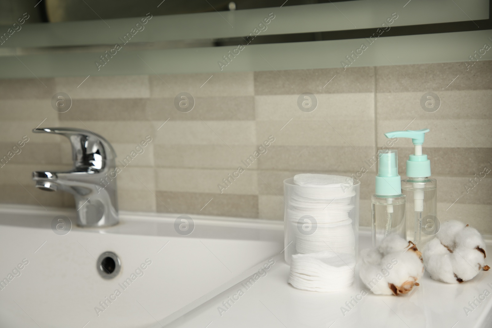 Photo of Cotton pads, cosmetic products and flowers on sink in bathroom